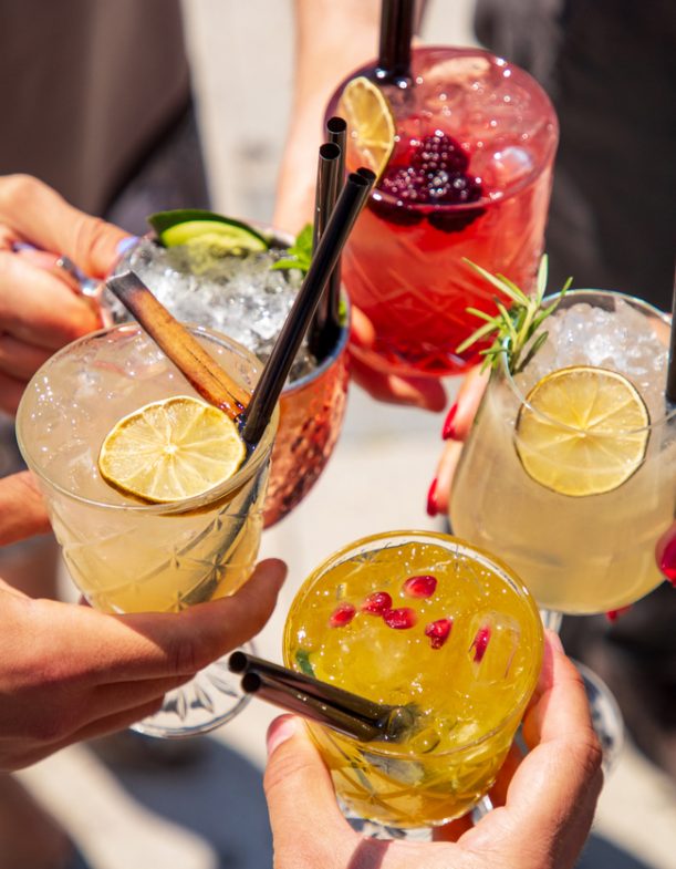 Five exotic cocktails on ice in hands joined in celebratory toast