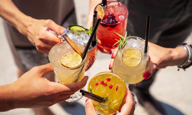 Five exotic cocktails on ice in hands joined in celebratory toast