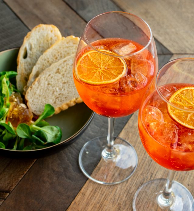 Italian aperitif aperol stpritz with ice and a slice of orange in large round glasses on a wooden table in a bar